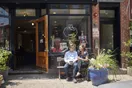 A corner bakery storefront on a busy pedestrian street with a display window and people walking past, in a natural documentary style.