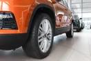 An aerial view of a used-car dealership lot on a busy commercial road with vehicles arranged in rows, in a documentary style.