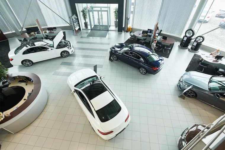 A wide view of a car rental lot near a busy road with hotels and an airport terminal in the background, in a natural documentary style.