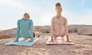 An empty sunlit yoga studio storefront with large street-facing windows and wood floors, shot in a natural documentary style.