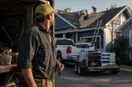 A roofing contractor at the open doors of a freshly equipped work vehicle in early-morning light, keys in hand, in a natural documentary style.