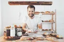A home baker sliding a sheet tray of pastries out of a residential oven in a bright kitchen, documentary style.