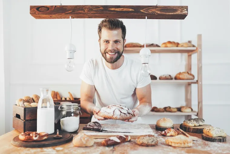 A home baker sliding a sheet tray of pastries out of a residential oven in a bright kitchen, documentary style.