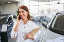 A used-car dealer walking a row of vehicles on a small lot, checking a phone, in a natural documentary style.