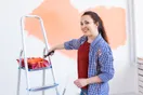 A house painter in white overalls cutting in a clean line along a ceiling with a brush, in a natural documentary style.