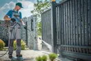 A pressure washing operator holding a surface cleaner on a driveway with a visible clean line splitting dirty from clean concrete, natural documentary style.