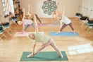 A yoga instructor rolling out mats in a sunlit studio before class, in a natural documentary style.