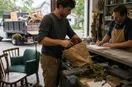 A junk removal operator unpacking new tools at a supply-house counter, in a natural documentary style.