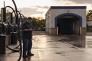 A car wash owner standing near the tunnel entrance at dusk, checking his phone beside the empty vacuum bays.
