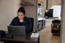A courier dispatcher checks an empty account-application inbox on a laptop inside a small warehouse office, in a natural documentary style.