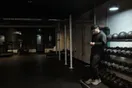 A gym owner sits alone in an empty studio at closing time checking an intro-booking calendar on a phone, in a natural documentary style.