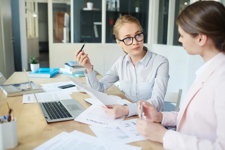 A firm owner reviewing work with a new staff accountant at a shared desk with two laptops, in a natural documentary style.