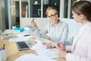 A firm owner reviewing work with a new staff accountant at a shared desk with two laptops, in a natural documentary style.