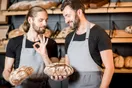 A bakery owner training a new employee at a decorating station with a printed checklist on the wall, in a natural documentary style.