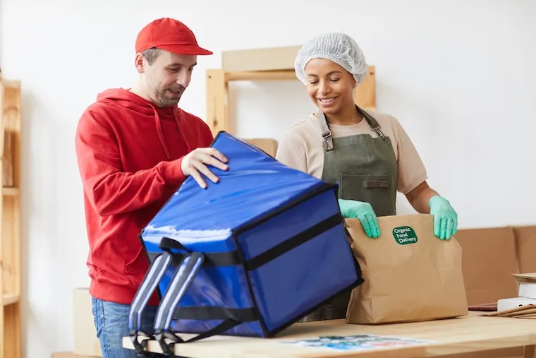 A delivery business owner going over a route checklist with a new driver beside a parked van, in a natural documentary style.