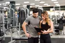 A gym manager reviewing a checklist on a clipboard with a new trainer on the gym floor, in a natural documentary style.