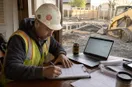 A site contractor signing registration paperwork at a table with a laptop open, in a natural documentary style.