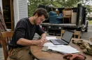 A junk removal operator signing registration paperwork at a table with a laptop open, in a natural documentary style.
