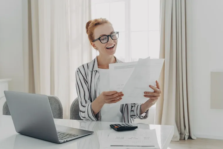 An accountant reviewing a profit-and-loss statement on screen with charts and a calculator on the desk, in a natural documentary style.