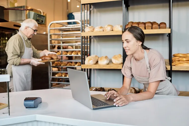 A bakery owner photographing a tray of decorated pastries with a phone for a social media post, in a natural documentary style.