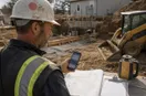 A site contractor checking a social feed on a phone at the job site, in a natural documentary style.