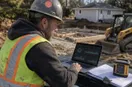 A site contractor studying a metrics dashboard on a laptop in natural light, in a natural documentary style.
