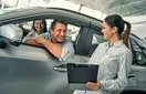A dealership salesperson texting a customer follow-up from a desk with a CRM open on screen, in a natural documentary style.
