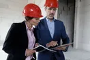A general contractor shaking hands with a client on a residential job site with a framed structure in the background, in a natural documentary style.