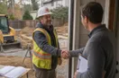 A site contractor shaking hands with a homeowner at the front door, in a natural documentary style.