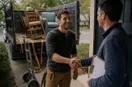 A junk removal operator shaking hands with a homeowner at the front door, in a natural documentary style.