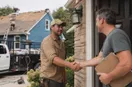 A roofing contractor shaking hands with a homeowner at the front door, in a natural documentary style.