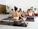 New students unrolling mats and chatting before a beginner yoga class in a bright studio, documentary style.