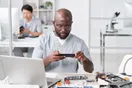A busy phone repair workshop with multiple technicians working at benches on disassembled devices, in a natural documentary style.
