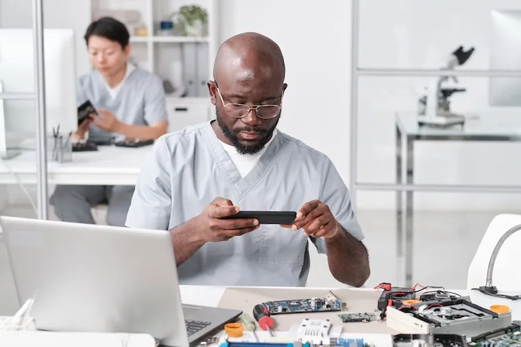 A busy phone repair workshop with multiple technicians working at benches on disassembled devices, in a natural documentary style.