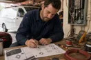 An electrician sketching logo concepts in marker on graph paper, in a natural documentary style.