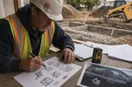A site contractor sketching logo concepts in marker on graph paper, in a natural documentary style.