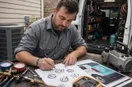 An HVAC technician sketching logo concepts in marker on graph paper, in a natural documentary style.