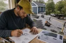 A roofing contractor sketching logo concepts in marker on graph paper, in a natural documentary style.