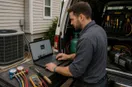 An HVAC technician reviewing a website mock-up on a laptop at the work site, in a natural documentary style.