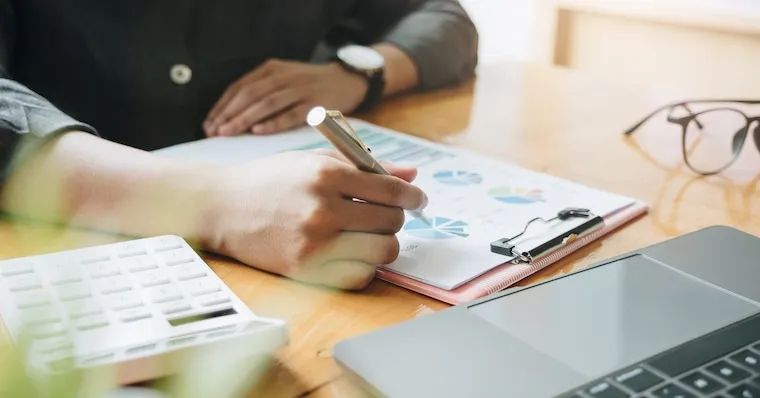 A designer's desk with logo sketches for an accounting firm, a laptop showing a wordmark, and color swatches in navy and gold, documentary style.