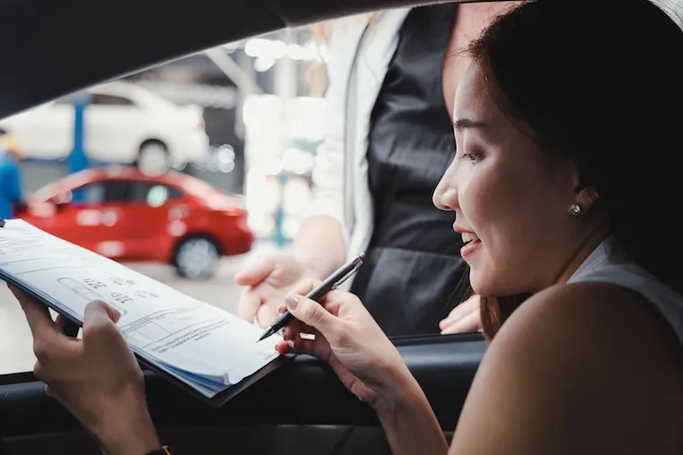 A car dealership logo displayed on a lot sign and a rear-window decal, shown in a natural documentary style.