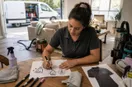 A cleaning business owner sketching logo concepts in marker on graph paper, in a natural documentary style.