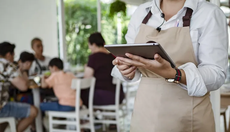A catering website open on a smartphone showing a food gallery and a Get a Quote button, held over a prep counter, in a natural documentary style.