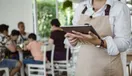 A catering website open on a smartphone showing a food gallery and a Get a Quote button, held over a prep counter, in a natural documentary style.