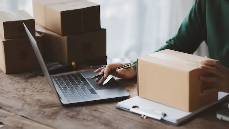 A laptop showing a courier company website with a coverage map and quote form, on a desk beside a delivery clipboard, in a natural documentary style.