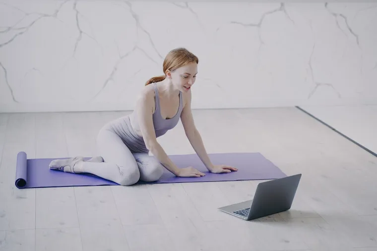 A yoga studio schedule and class booking page open on a laptop and a phone side by side, in a natural documentary style.