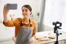 A baker filming an overhead shot of cookie dough being scooped onto a tray with a phone mounted above the counter, in a natural documentary style.