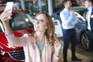 A salesperson filming a short vertical video beside a car on a dealership lot, shown in a natural documentary style.