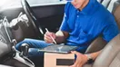 A courier checking a smartphone beside a delivery van in a parking lot, in a natural documentary style.