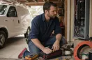 An electrician installing a yard sign at the curb of a finished job, in a natural documentary style.